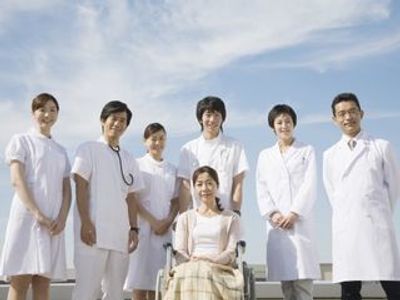 医師・看護師に囲まれて笑顔で写真に納まる女性。車いすに乗っている様子