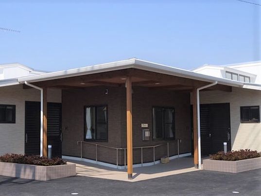 平屋建ての建物の中央の玄関には屋根が付き、花壇も複数設置されている。敷地内には広い駐車スペースもある。