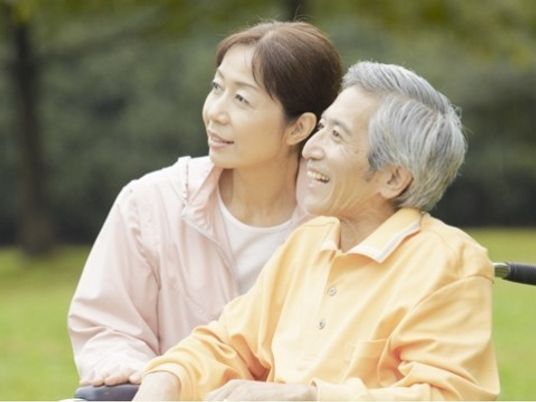 柔らかな表情で付き添う人とほほ笑む高齢者。外に出て自然を眺めている様子がうかがえる。自然な笑顔を印象的。