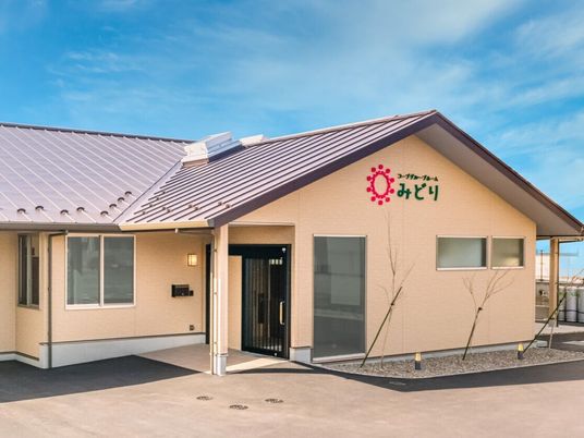 ホーム名が書かれた外壁はブラウン系で、グレーの屋根が付いた平屋建ての建物。