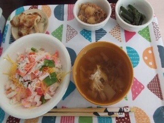 カラフルなトレーの上には汁物やちらし寿司、野菜の和え物、肉のソテーなどがある。
