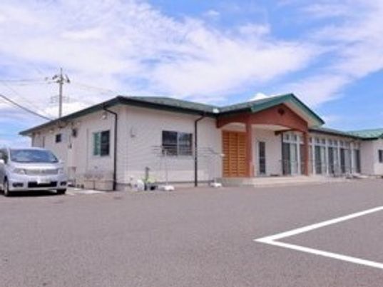 広い敷地内にはグリーンの屋根が付いている平屋建ての建物があり、グレーの車が止まっている。