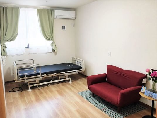 赤いソファと介護用ベッド、テーブルが並べられている日当たりの良い部屋