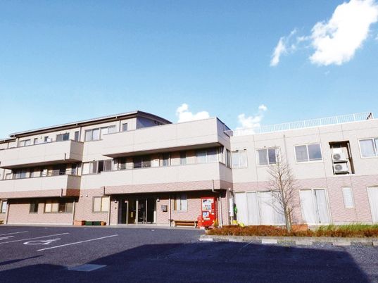 青空のもとに３階建ての建物が写っている様子。駐車場スペースもある