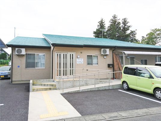 緑色の屋根とスロープ付きの玄関が印象的な平屋建ての建物。駐車場スペースがある広め庭もある