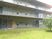 広い庭には芝生が敷かれ、各フロアにベランダが付いた3階建ての建物がある。庭には木も植えられている。