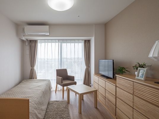 たんすとベッド、いす、テーブルが並んでいる施設の部屋の様子。コーディネートの一例