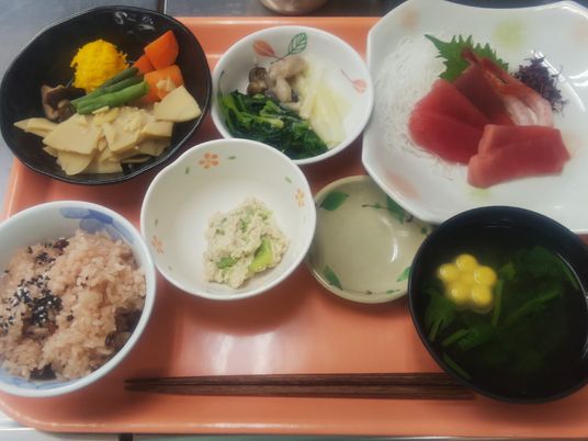 赤飯やマグロの刺身、吸い物、煮物、あえ物などが並べられたオレンジのトレー。