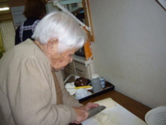 野菜をまな板の上で切っている女性入居者の様子。家庭的な雰囲気のキッチン。