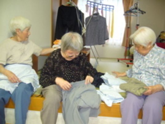 3人の女性入居者が並んで洗濯物をたたんでいる様子。