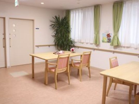 椅子と机が複数組並んでいる施設内のリビングの様子。窓がある明るい部屋