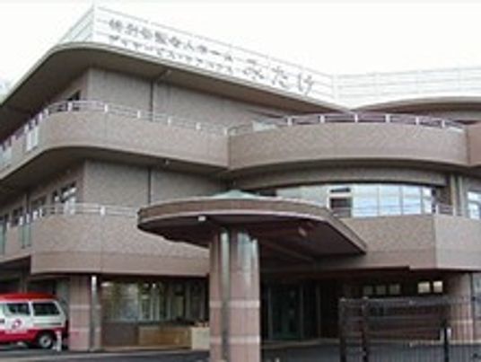 ブラウン系の外壁の3階建ての建物の玄関先には大きな車寄せが付き、各フロアにベランダがある。