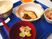 麩が浮いた吸い物や白いご飯、煮物に焼き魚、カットフルーツなどが並んだブルーのトレー。