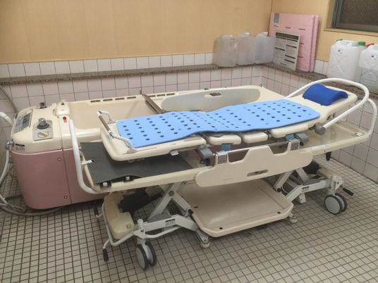 ピンクの寝台浴が置かれた浴室は白いタイルが貼られている。