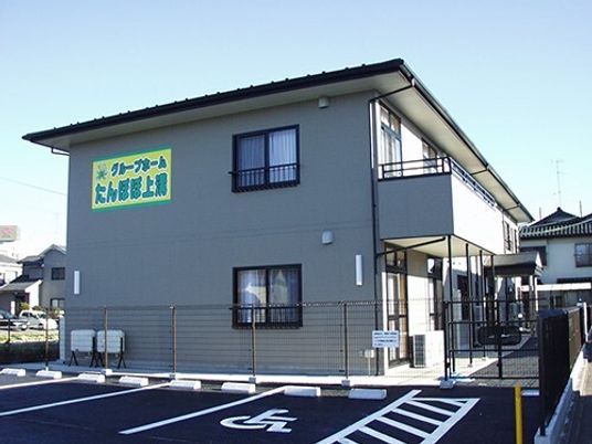 ライトグレー系の外観の２階建ての建物は日当たり良好で2階部分にベランダがあり、ホーム名が書かれた看板が外壁に付いている。
