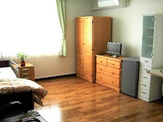 フローリングの部屋。大きな窓にはカーテンが付き、ベッドやエアコン、収納家具もある。