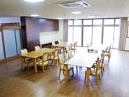 木製のダイニングテーブルが複数置かれ、大きな窓がたくさんあり、明るい雰囲気。