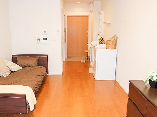 介護用ベッドとタンス、洗面台や玄関が写った施設内の居室の写真