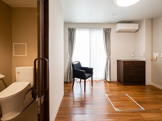 フローリングの部屋にはいすやタンスが置かれ、緊急通報装置が付き、引き戸が付いたトイレもある。