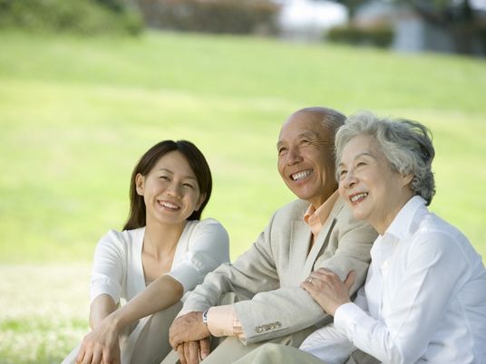 笑顔で語り合う高齢者夫婦と女性スタッフ。日当たりのいい芝生の上に並んで座っている。