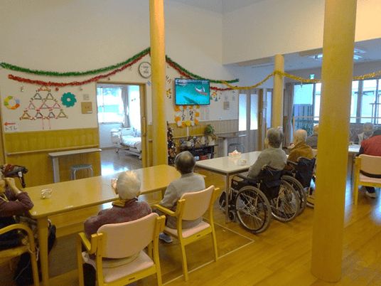飾り付けが施された施設内の壁とテレビを見ている高齢者の様子