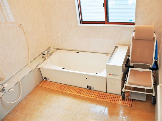 洗い場が広く、シャワーや浴室用車いすを設置。白い浴槽が窓のそばにある。