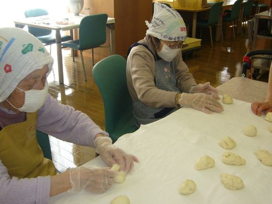 エプロンや三角巾をして熱心にパンをこねている入居者の様子。