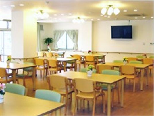四人掛けのテーブルと椅子が並んでいる施設内のリビングの様子。食事をとるための広めのホール