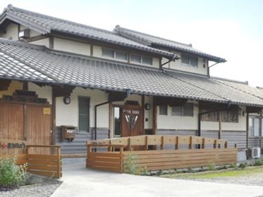 グレーの瓦屋根が付いた平屋建ての建物。平屋建ての建物は一部2階建てで庭もある。