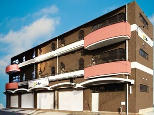 ブラウンを基調とした3階建ての建物。ベランダが付き、白いラインがある。