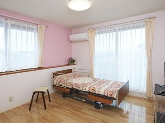 寝具付きベッドが置かれたフローリングの部屋にはエアコンがあり、大きな窓がある。