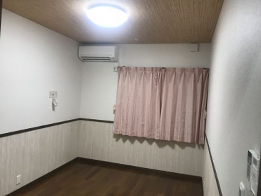 居室のピンクのカーテンが設置された窓の横にはエアコンもある。