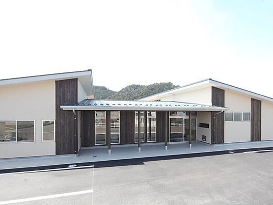 平屋建ての建物の中央の玄関には屋根が付き、駐車スペースもある。