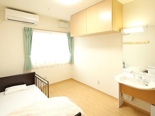 天井に近い壁に設置された収納、ベッドや洗面所が付いたフローリングの居室。