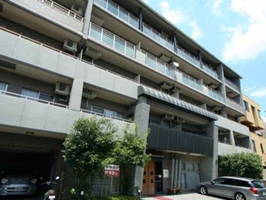 横に長い建物には各フロアにベランダが付き、建物の前には木が植えられ駐車スペースがある。