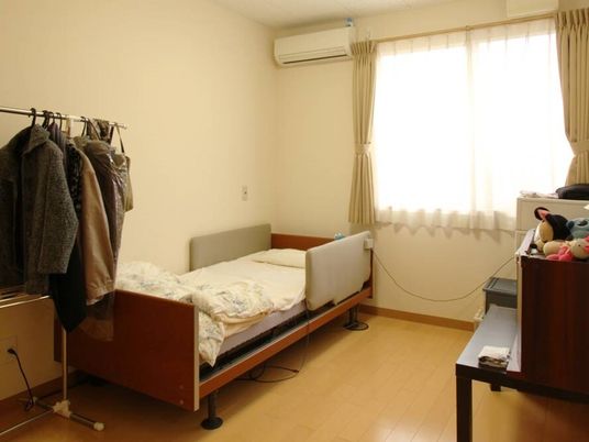 エアコンが付いたフローリングの部屋には介護ベッドやハンガーラックが置かれ、おおきな窓がある。