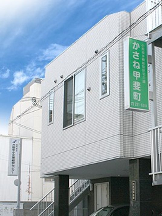 白い建物の1階部分は駐車スペースとなっていて、外壁には緑の看板がかかっている。