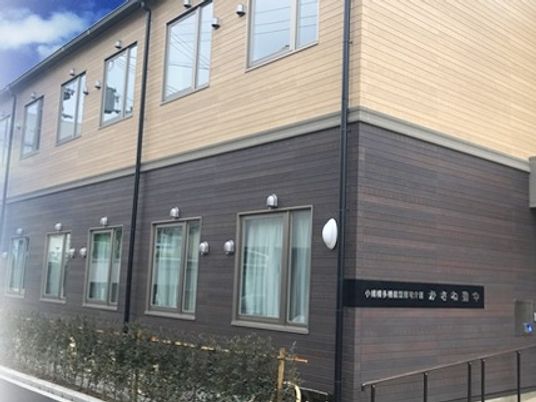 2階建ての建物は2階部分がベージュ、1階部分がブラウンという2色使い。建物のすぐ横に生垣がある。