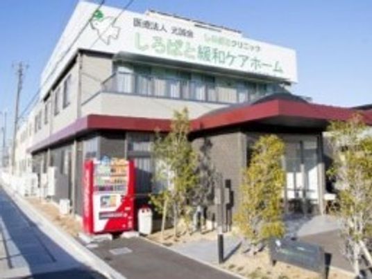 自動販売機が設置されている敷地内には沢山の木が植えられている。2階建ての建物はグレー系の外観。