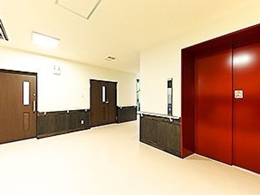 広い廊下から続いているエレベーターホール。赤いエレベーターの扉は認識しやすい。