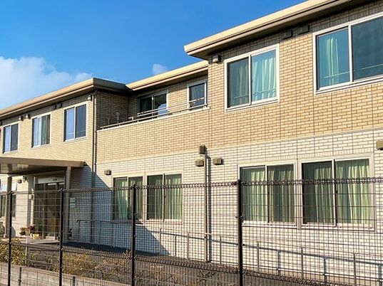ベージュの2階建ての建物は周囲にフェンスが建てられ、2階部分にはテラスが設置されている。