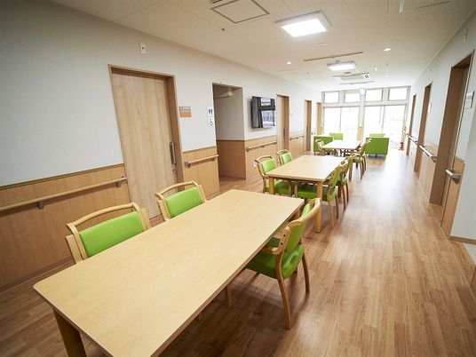 長机と椅子が並べられている施設内の廊下とリビング。奥の方に窓があるリラックススペース