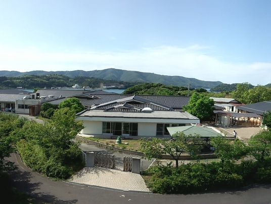 緑に囲まれた和風の建物は平屋建て。奥には山が連なっている姿が見える。