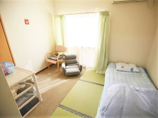 畳が敷かれた居室には布団があり、窓際にはいすが二つ並んでいる。