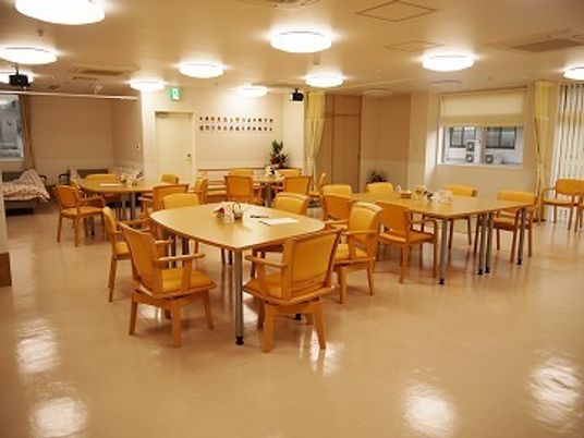 木製のダイニングテーブルが並び、いすがセットされた食堂。明るい雰囲気で奥には静養室がある。