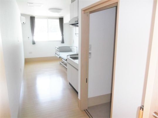 出入り口から居室を見渡した様子。ベッドやキッチン、トイレのドアが見える。