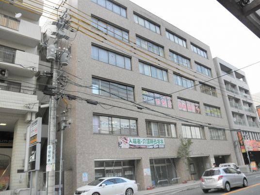 茶色とベージュの2階建ての建物。周りには木が植えられ、テーブルセットも置かれている。