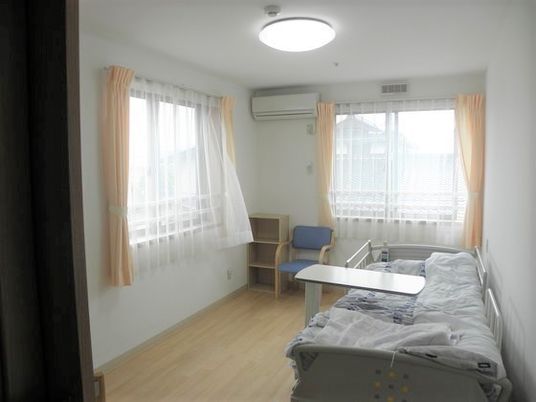フローリングのシンプルな個室の部屋には窓が二つあり、ベッドやエアコン、いすと棚が付いている。