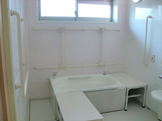 壁一面に手すりが取り付けられている様子。一人用の浴槽と腰掛がある介護浴槽