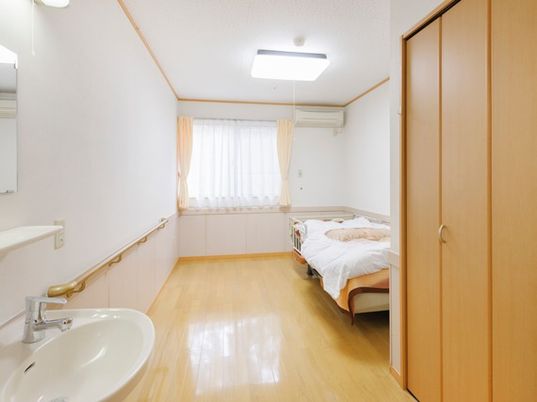 エアコン付きのフローリングの居室には収納家具や洗面所、ベッドもある。